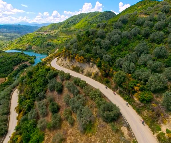 Group riding electric bikes through green hills and rural roads near Berat on the way to Roshnik.
